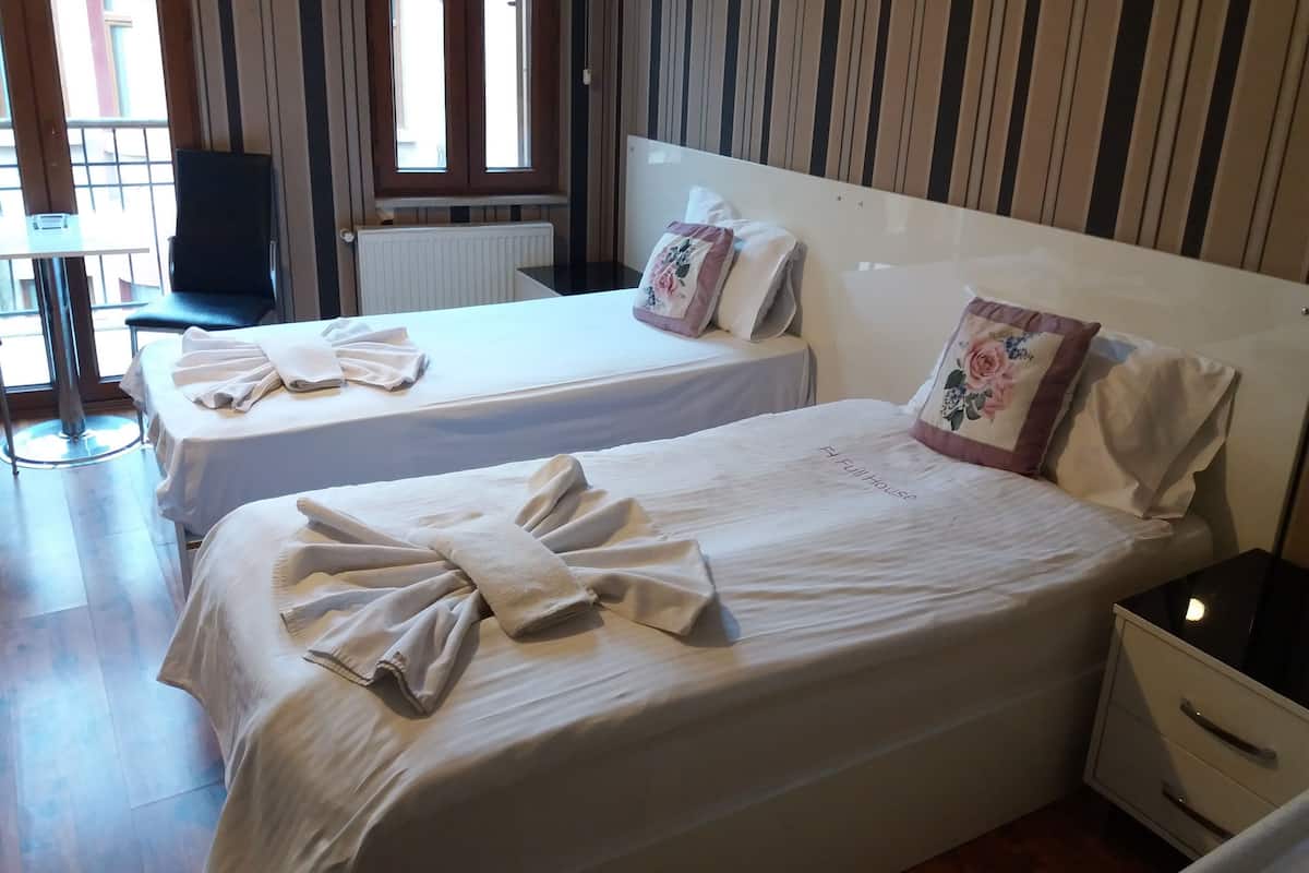Ein Hotelzimmer mit zwei Einzelbetten, einem kleinen Tisch, einem Stuhl und einem Fenster mit vertikalen Jalousien.