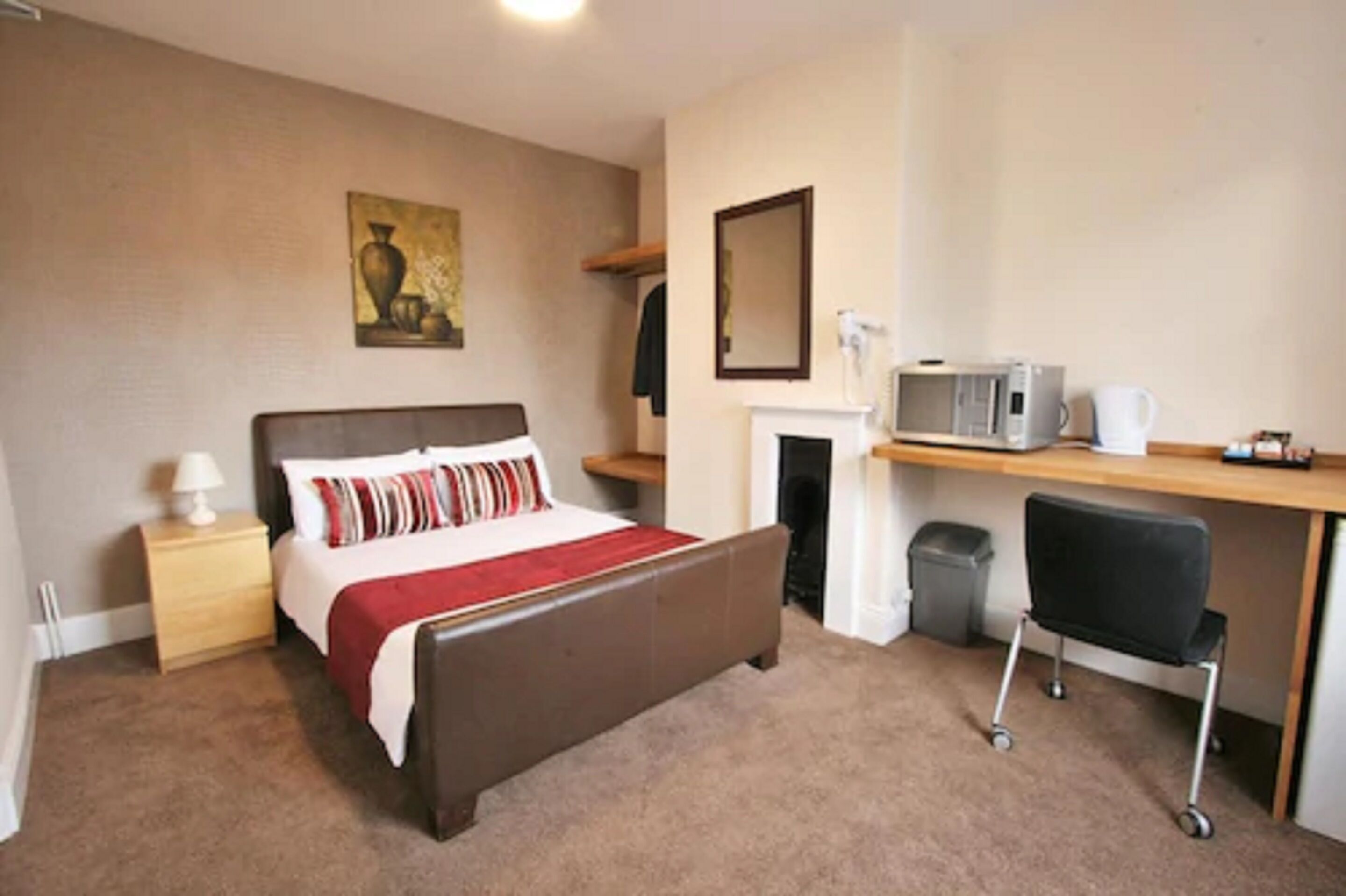 A bedroom with a bed, bedside table, lamp, and a desk with a chair.