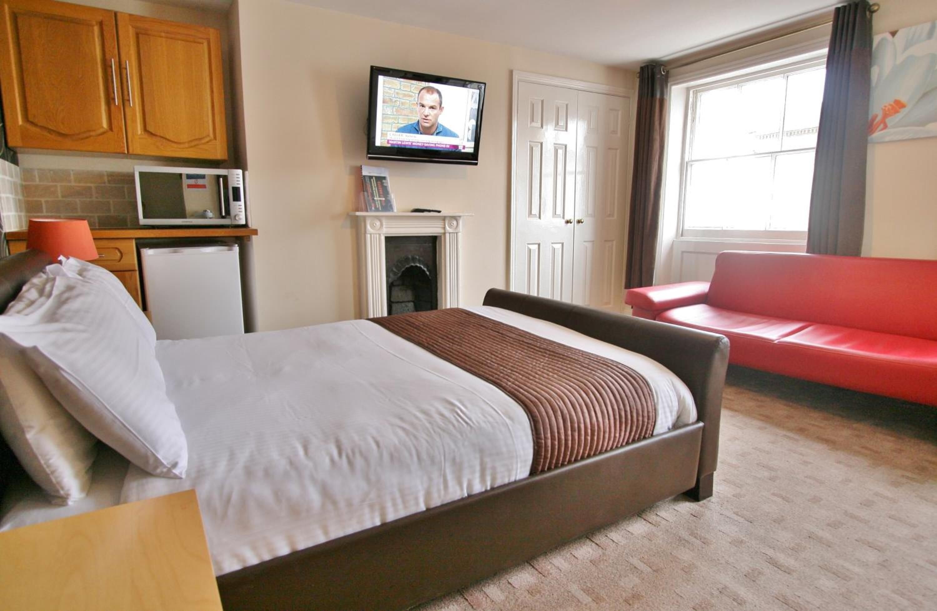 A hotel room with a bed, a red sofa, a TV, a microwave, and a fireplace.