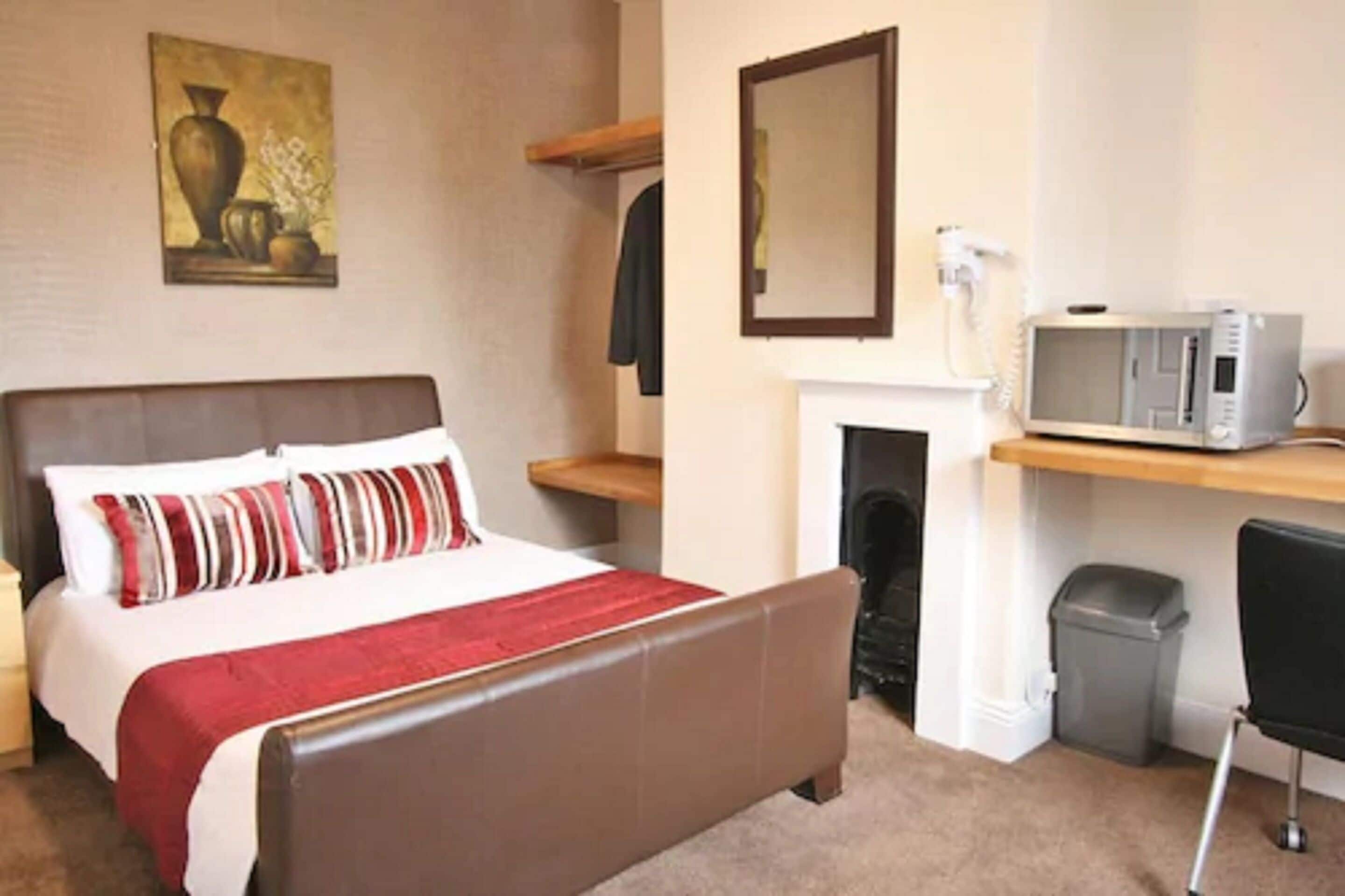 A hotel room with a bed, a microwave, a fireplace, a trash bin, and a chair.
