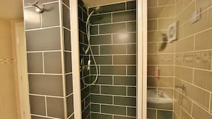Une salle de bain avec des murs recouverts de carreaux foncés, une douche avec un pommeau de douche amovible et un lavabo avec un robinet.