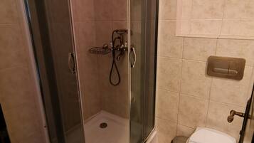 Ducha con puerta de vidrio, inodoro y perchero.