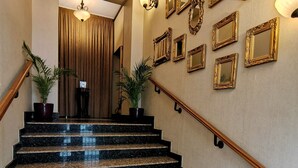 Una imponente escalera de granito, flanqueada por plantas en macetas y espejos montados en la pared.