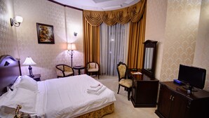 Una habitación de hotel con cama, dos sillones, un escritorio, televisor y lámpara.