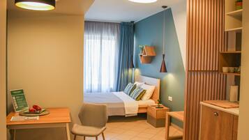 Ett modernt hotellrum med en säng, ett skrivbord, en stol, ett nattduksbord och en garderob i trä.