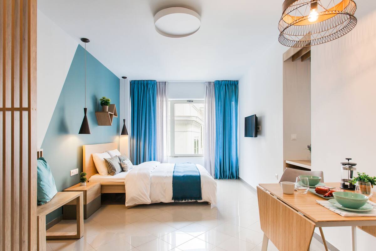 A modern bedroom with a bed, bedside tables, a desk, and a window with curtains.