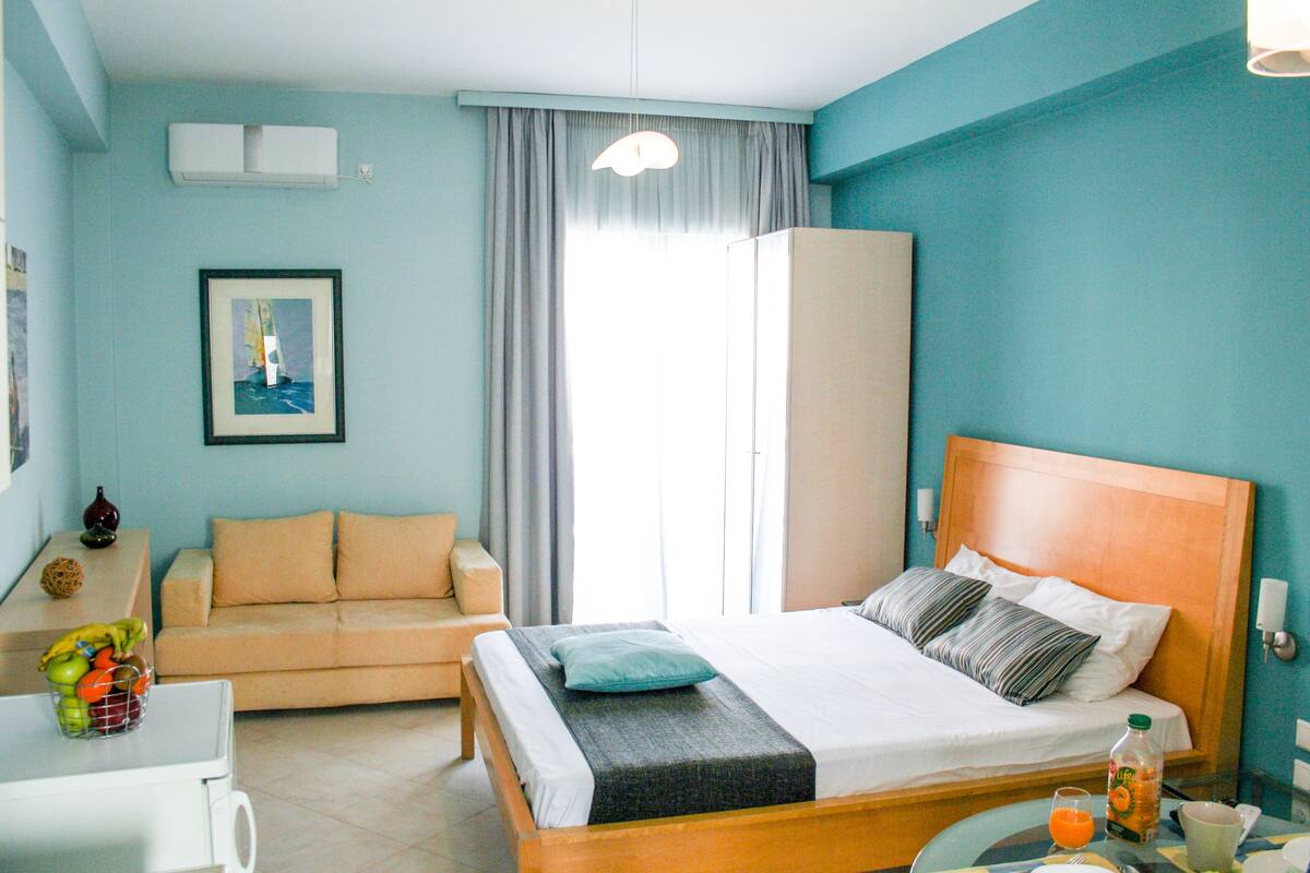 A hotel room with a bed, a sofa, a table with a fruit basket, a bottle of orange juice, and a framed picture on the wall.