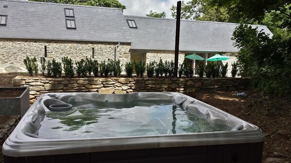 A hot tub in a backyard with a stone wall and a house in the background. - Rhostwarch Bed and Breakfast (Crymych)