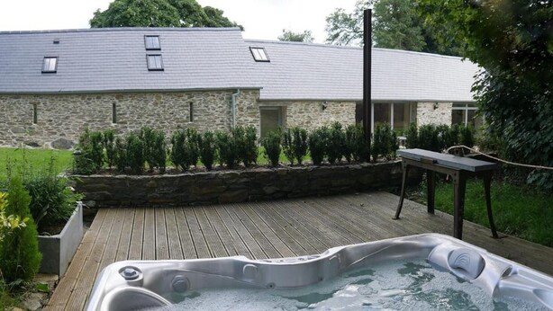 Un bâtiment en pierre doté d’un toit en pente, d’un jacuzzi et d’une terrasse en bois.