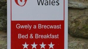 Une enseigne indiquant « Cymru Wales » et proposant un service de « chambre d’hôtes et petit-déjeuner » (Gwely a Brecwast), avec une note de quatre étoiles.