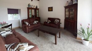 A living room with a brown sofa, a coffee table, and a cabinet with decorative items. - Rhostwarch Bed and Breakfast (Crymych)