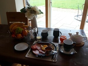 A breakfast table with a plate of eggs, bacon, and tomatoes, a bowl of fruit, and a vase of flowers.