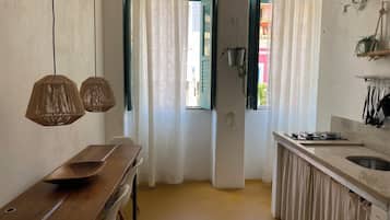 Una cocina con una mesa de madera, dos lámparas colgantes, un ventanal con cortinas y una planta suspendida.