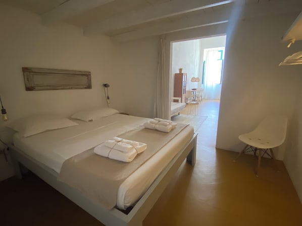 Une chambre d’hôtel propre et moderne, dotée d’un grand lit, d’une table de chevet, d’une chaise et offrant une vue sur la salle à manger.