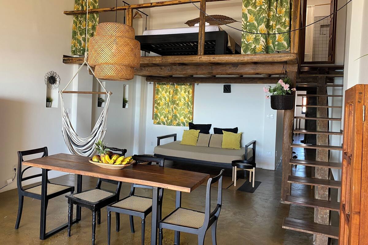 A dining area with a wooden table and chairs, a hanging rattan light fixture, and a view of a bedroom with a bunk bed.