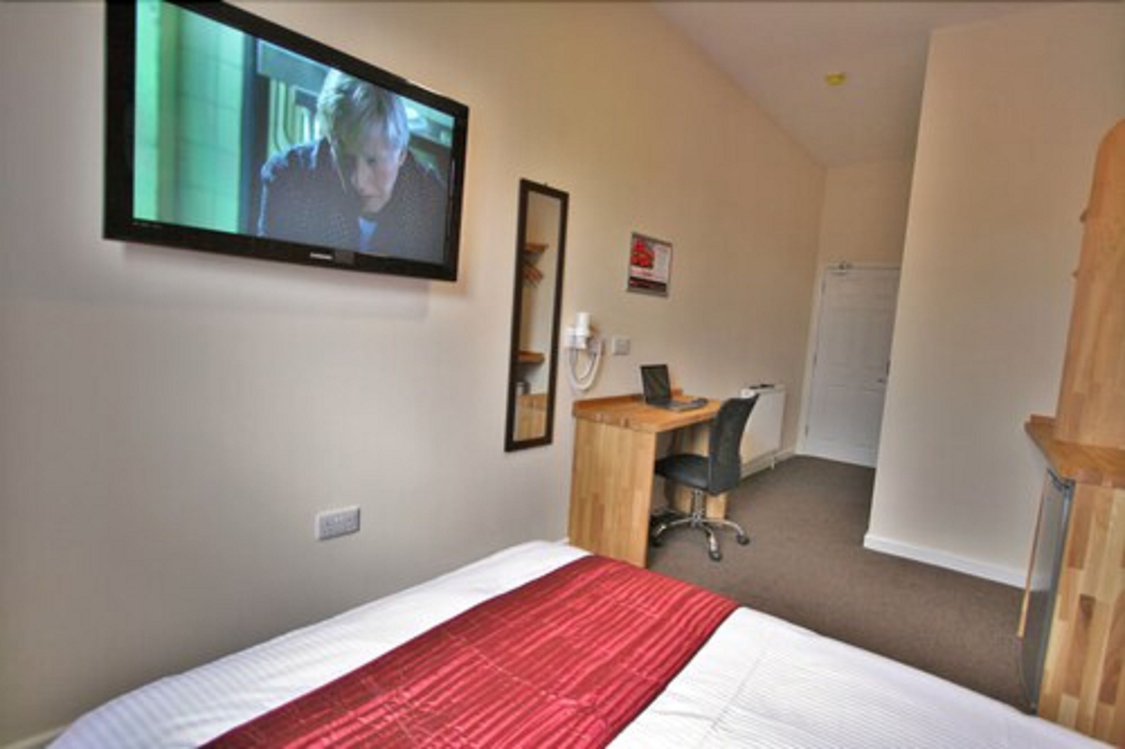 A hotel room with a bed, a desk, a chair, a television mounted on the wall, and a mirror.