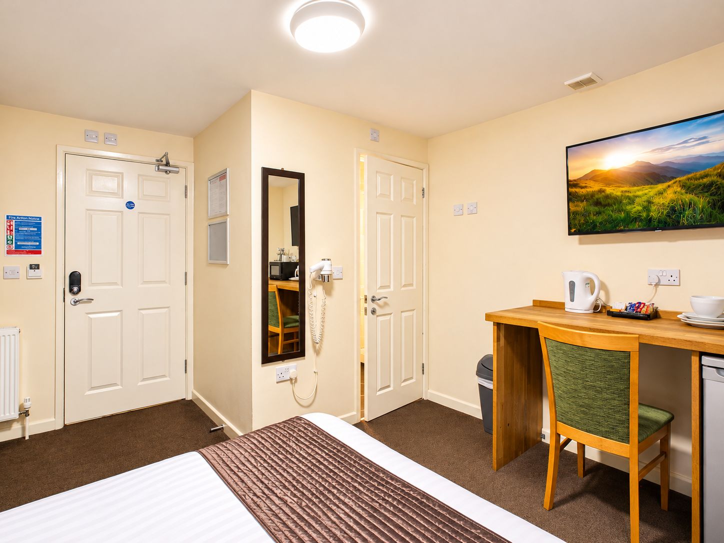 A hotel room with a bed, a desk with a chair, a telephone, a picture on the wall, and a window.