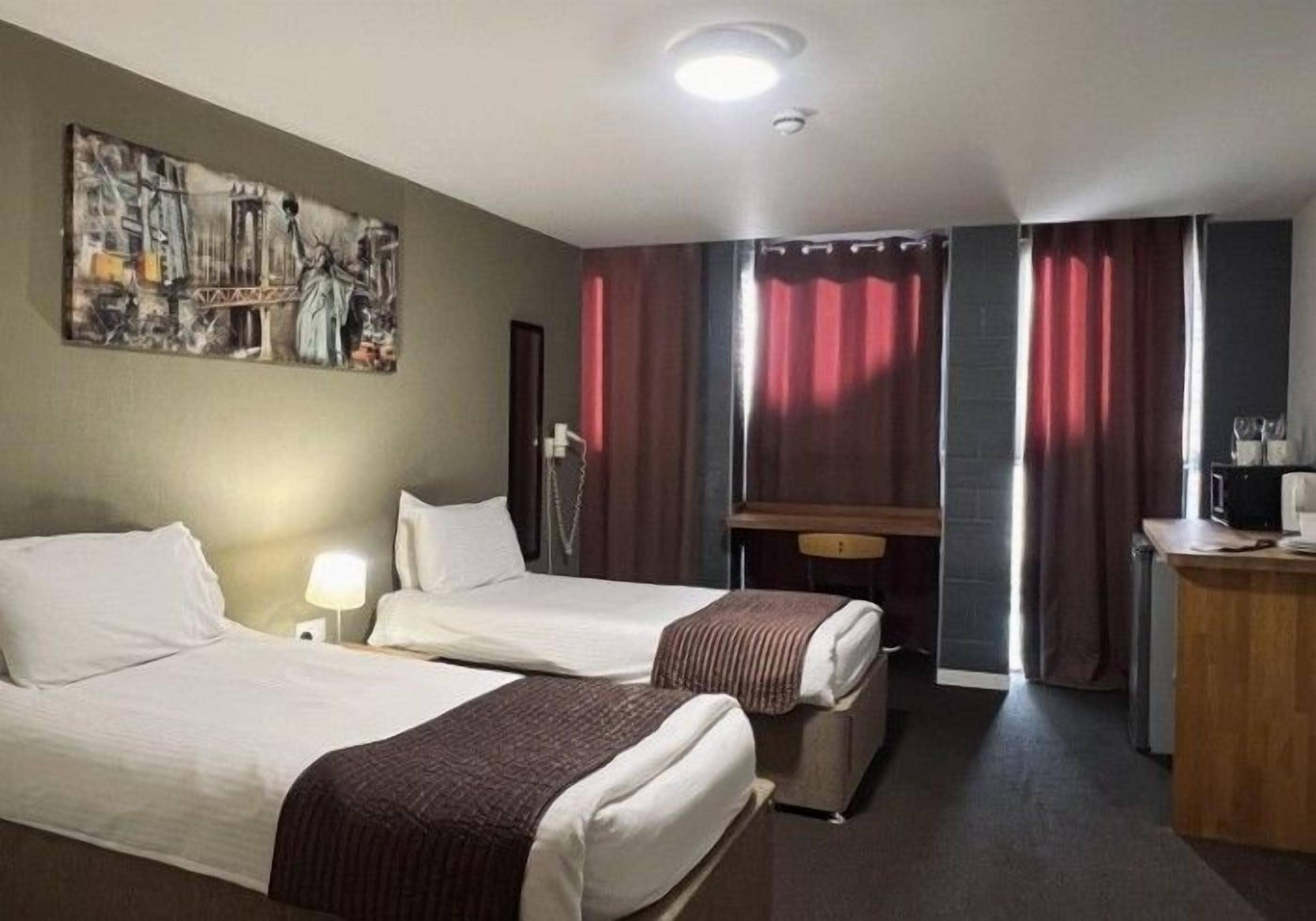 Ein Hotelzimmer mit zwei Betten, einem Schreibtisch, einem Stuhl und einem Bild an der Wand.