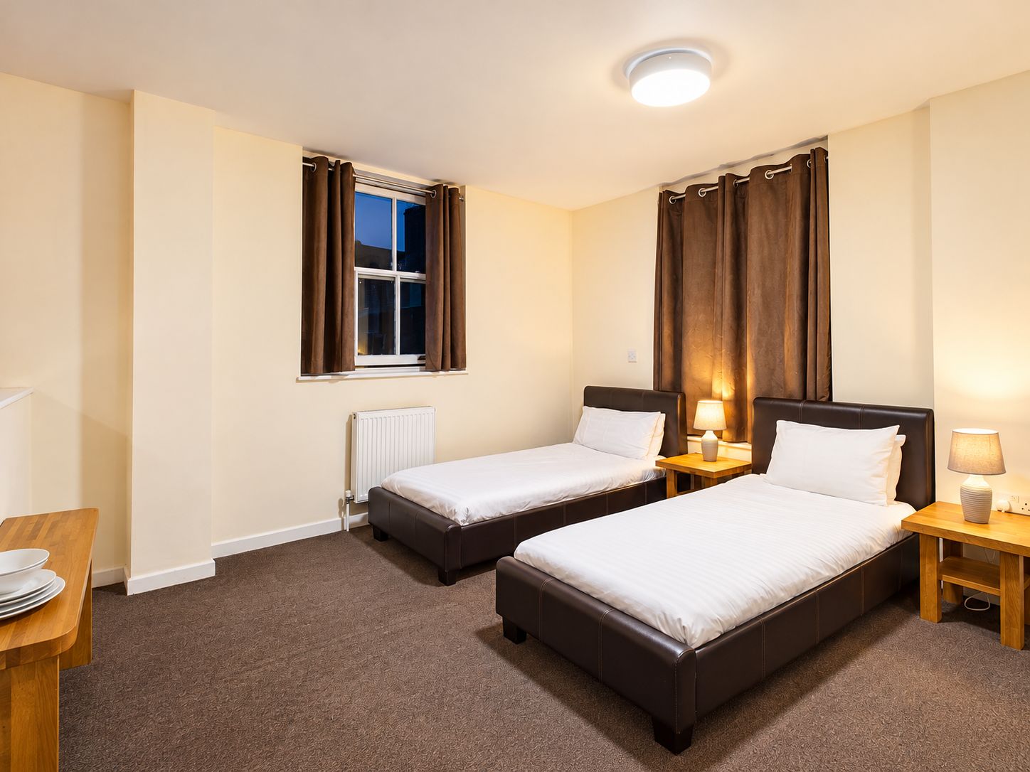 Habitación de hotel con dos camas, una ventana con cortinas, un radiador y lámparas de noche.