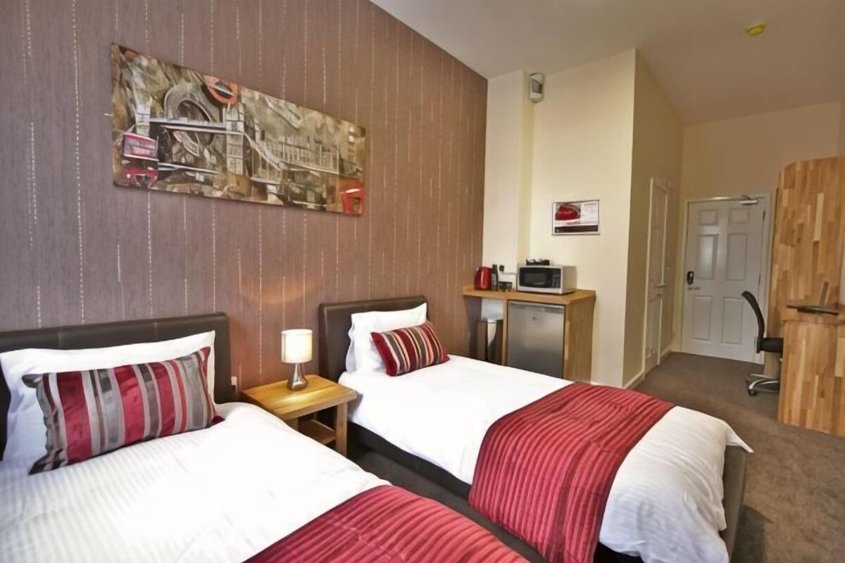 A hotel room with two beds, a desk with a lamp, a microwave, and a door.