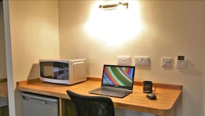 A compact kitchenette with a microwave, a laptop, and a coffee mug on a wooden countertop. - Homesly Gloucester Hotels Ltd. (Gloucester)