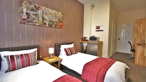 A hotel room with two beds, a desk with a lamp, a small TV, and a door. - Homesly Gloucester Hotels Ltd. (Gloucester)