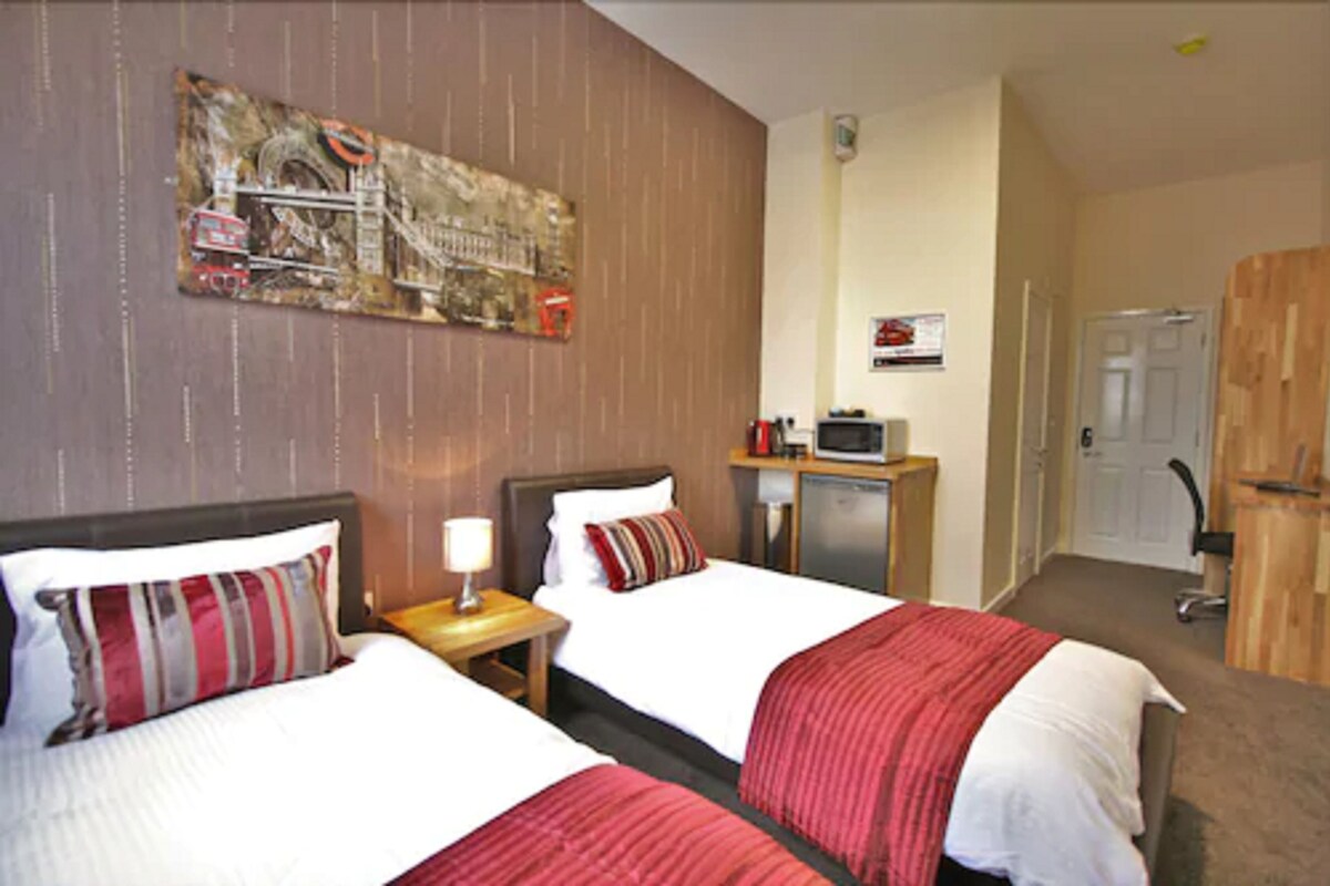 Een hotelkamer met twee bedden, een bureau met een lamp, een kleine televisie en een deur.