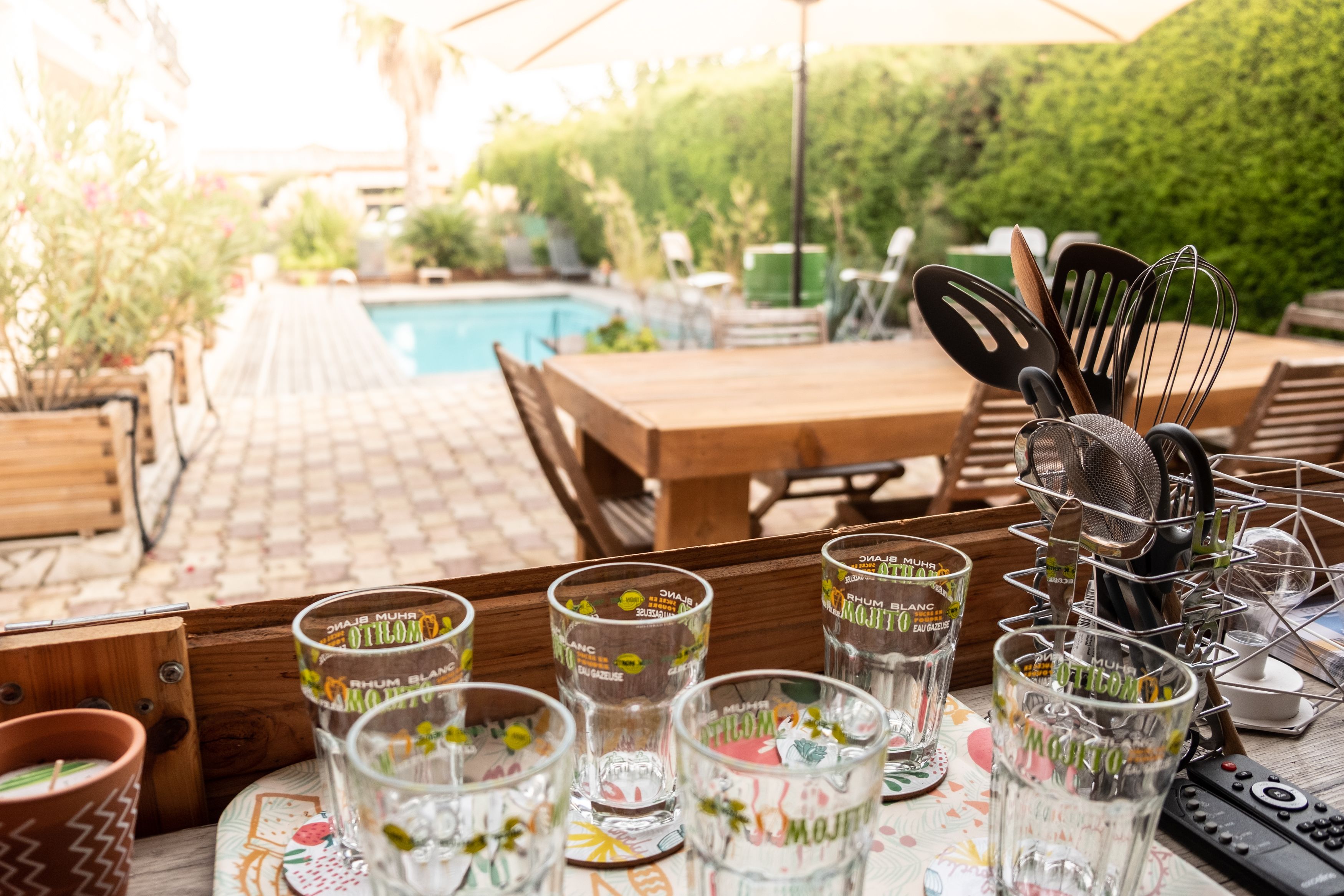 A poolside area with a wooden table, several shot glasses, and a utensil holder.