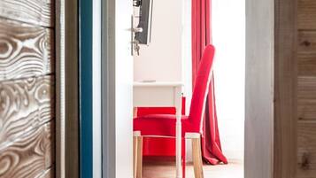 A room with a wooden floor, a red chair, a white wall-mounted TV, and a red curtain.