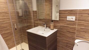 A modern bathroom with a glass shower enclosure, a white sink, and a dark wooden vanity.