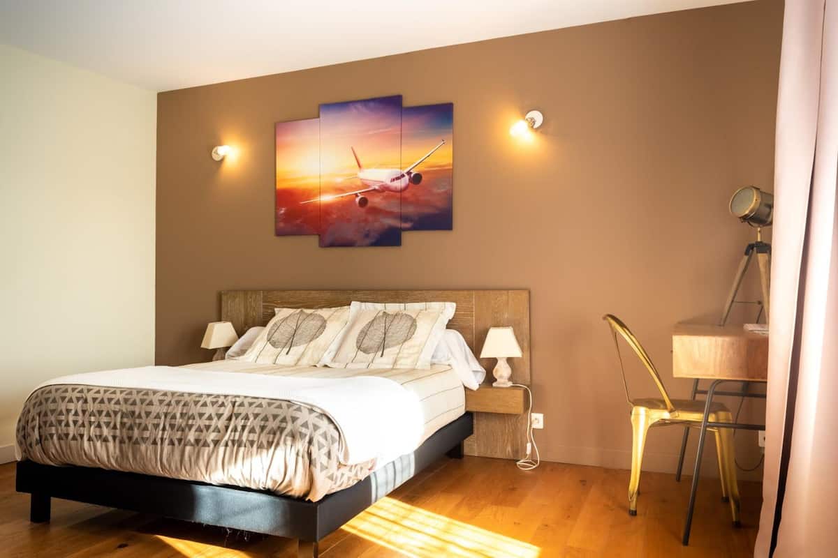 A bedroom with a bed, a desk with a lamp, and a painting of an airplane on the wall.