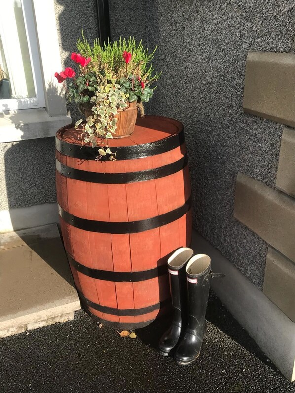A wooden barrel planter with a potted plant and red flowers, placed on a concrete surface next to a building.