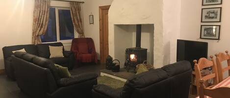 A cozy living room with a fireplace, two black sofas, a red chair, and a wooden table with a checkered tablecloth.