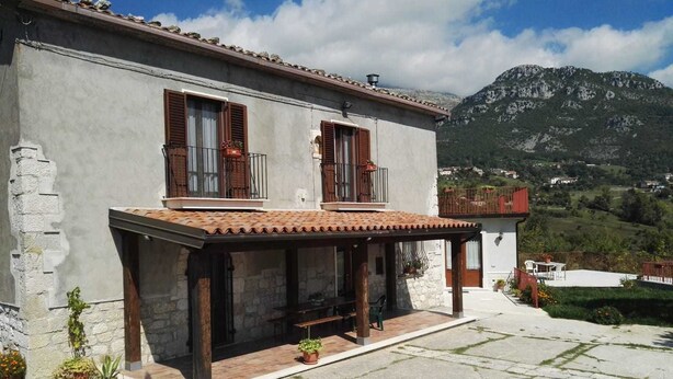 Un bâtiment à deux étages doté d’un balcon, de murs en pierre et surplombant un paysage montagneux.