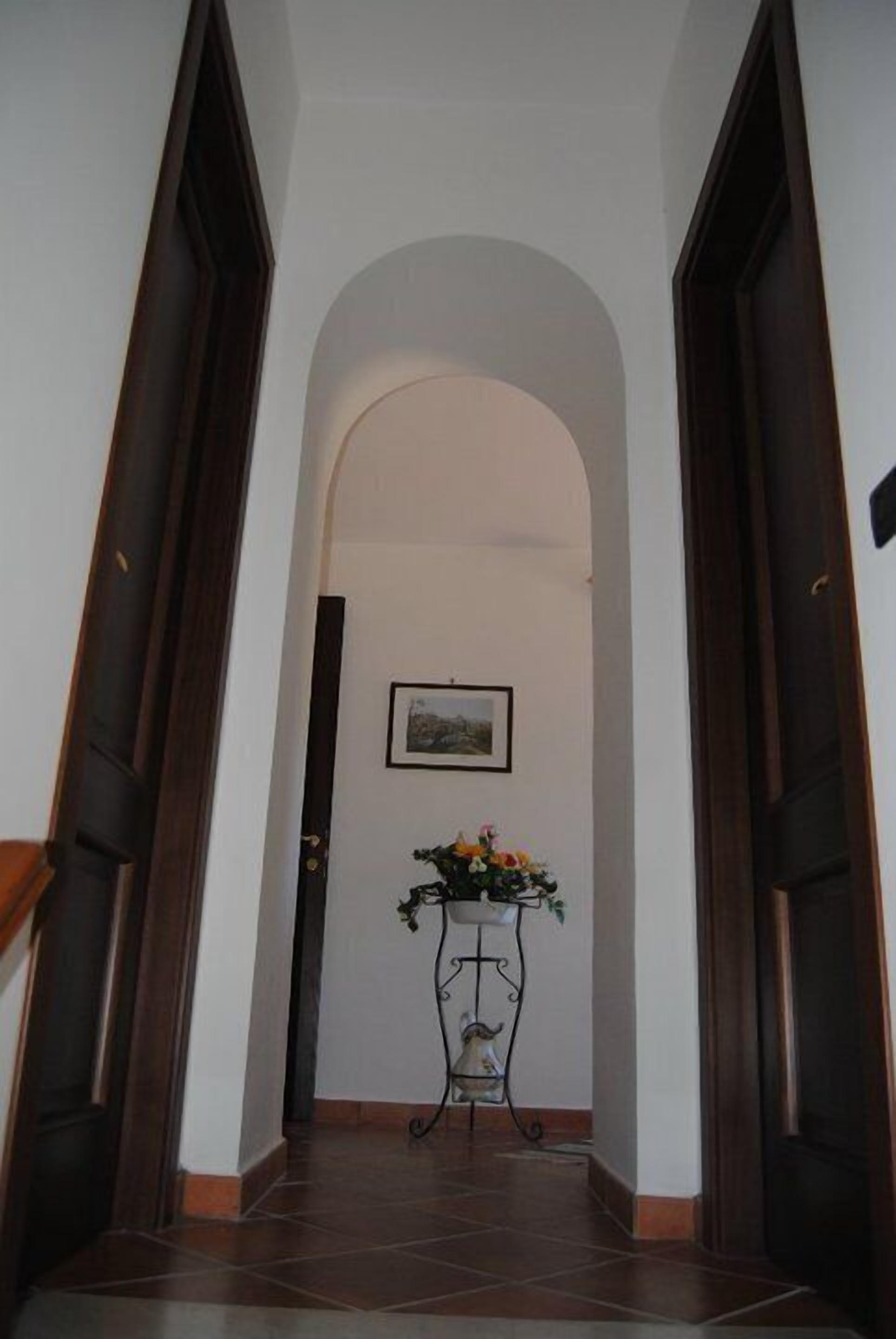 A hallway with a tiled floor, an arched doorway, and a small table with a flower arrangement.