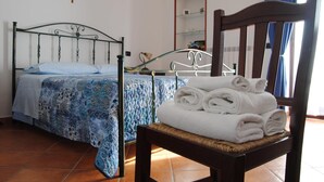 Une chambre à coucher avec un lit, une chaise sur laquelle sont posées des serviettes, un crucifix au mur et un miroir.