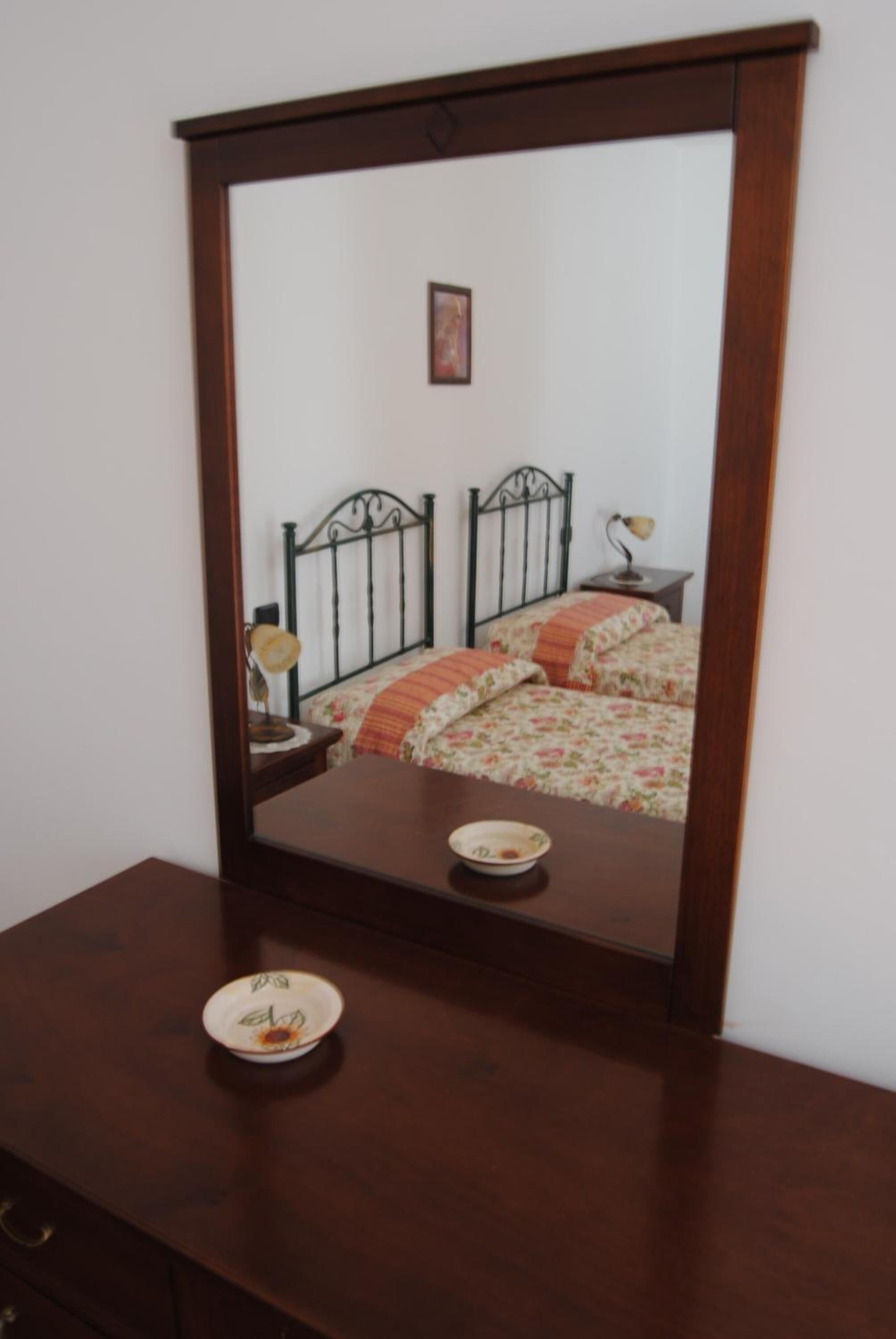 Una camera da letto con una struttura letto in legno, un comodino, una lampada e uno specchio che riflette l'ambiente.