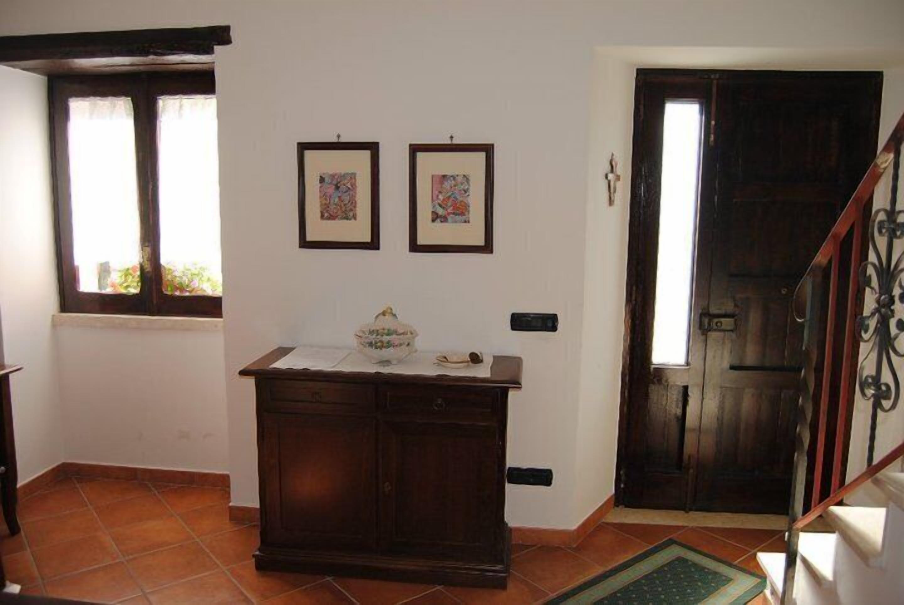 A room with a wooden cabinet, two framed artworks on the wall, a door, and a window with a view of greenery outside.