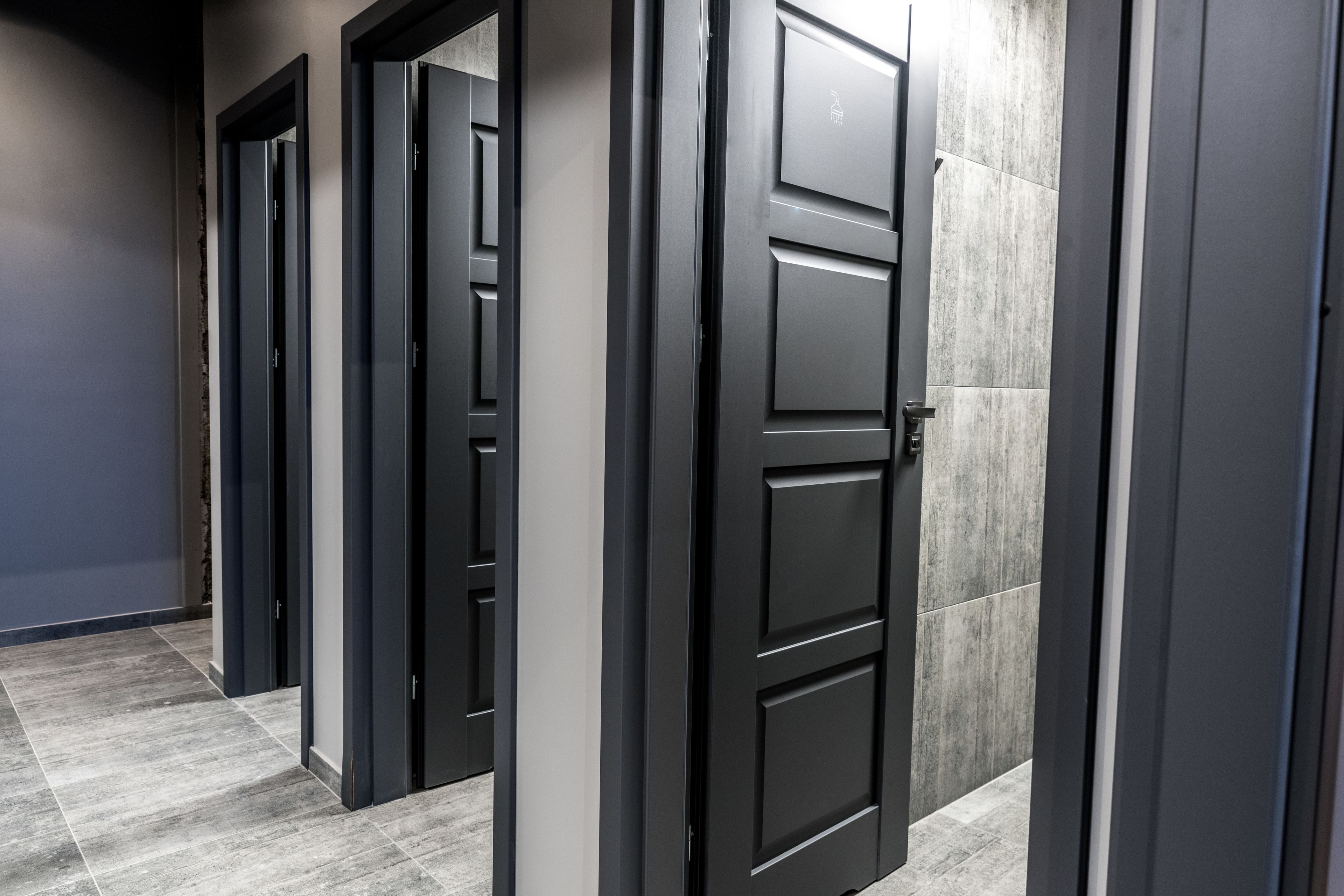A hallway with multiple black doors, grey walls, and grey tiled flooring.