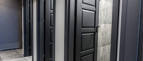 Un pasillo con varias puertas negras, paredes grises y suelo de baldosas grises.