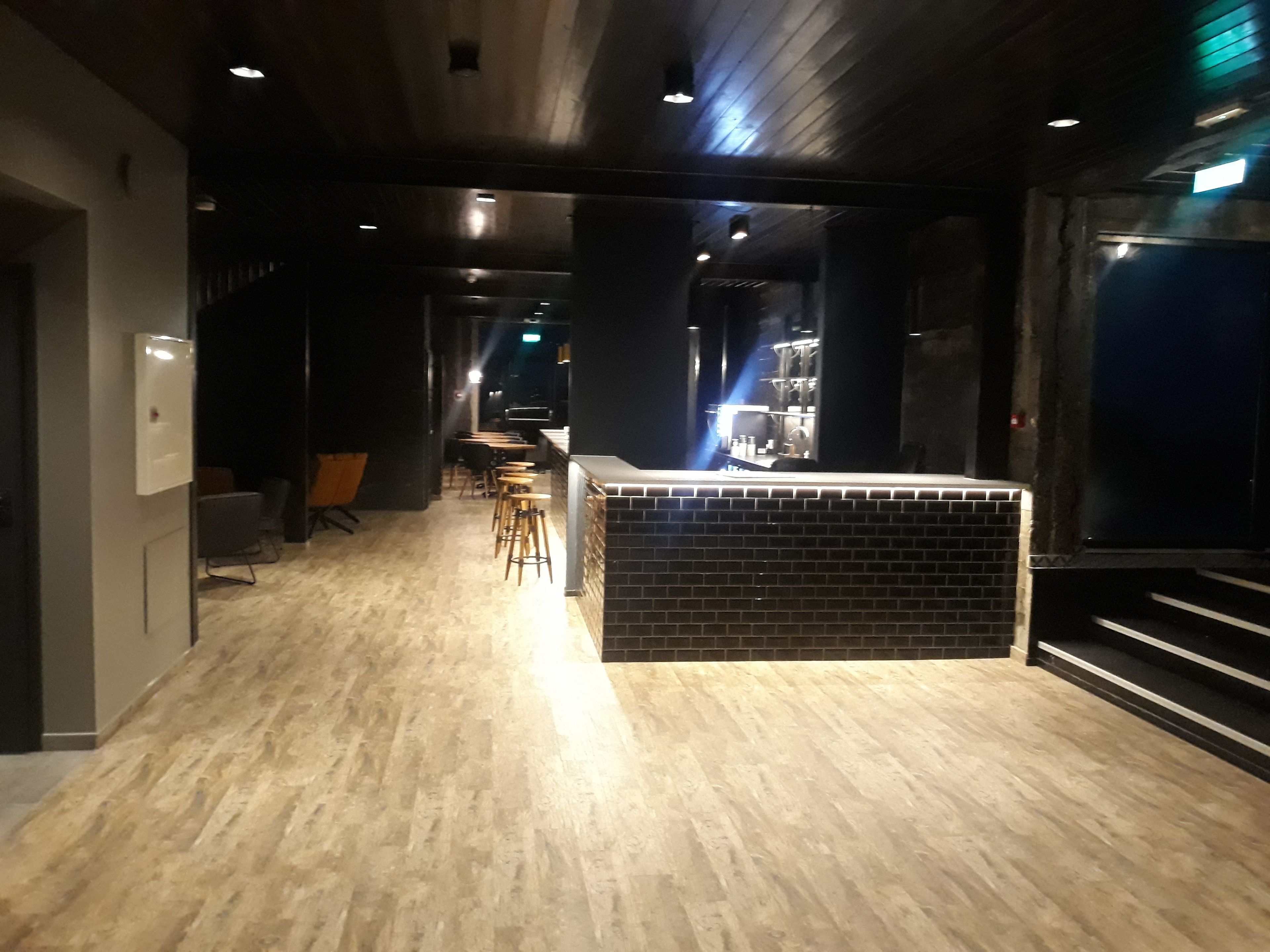 Un interior moderno con mostrador de recepción, suelo de madera y zona de bar.