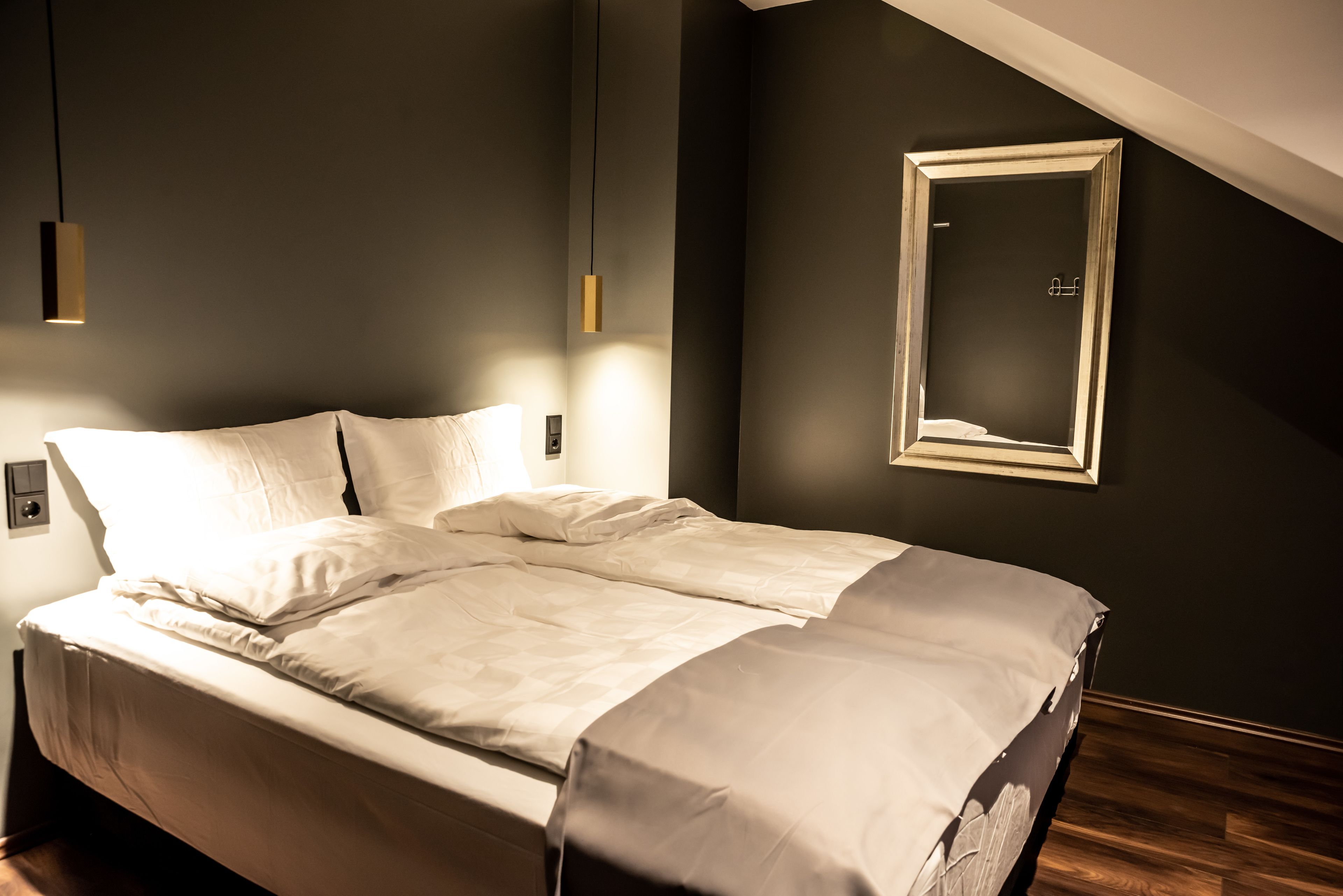 Een net opgemaakt bed in een kamer met donkere wanden, een houten vloer en een lijst met spiegel.