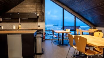 Una cocina moderna con un amplio ventanal con vista al océano, mesas y sillas de madera, y un refrigerador pequeño.