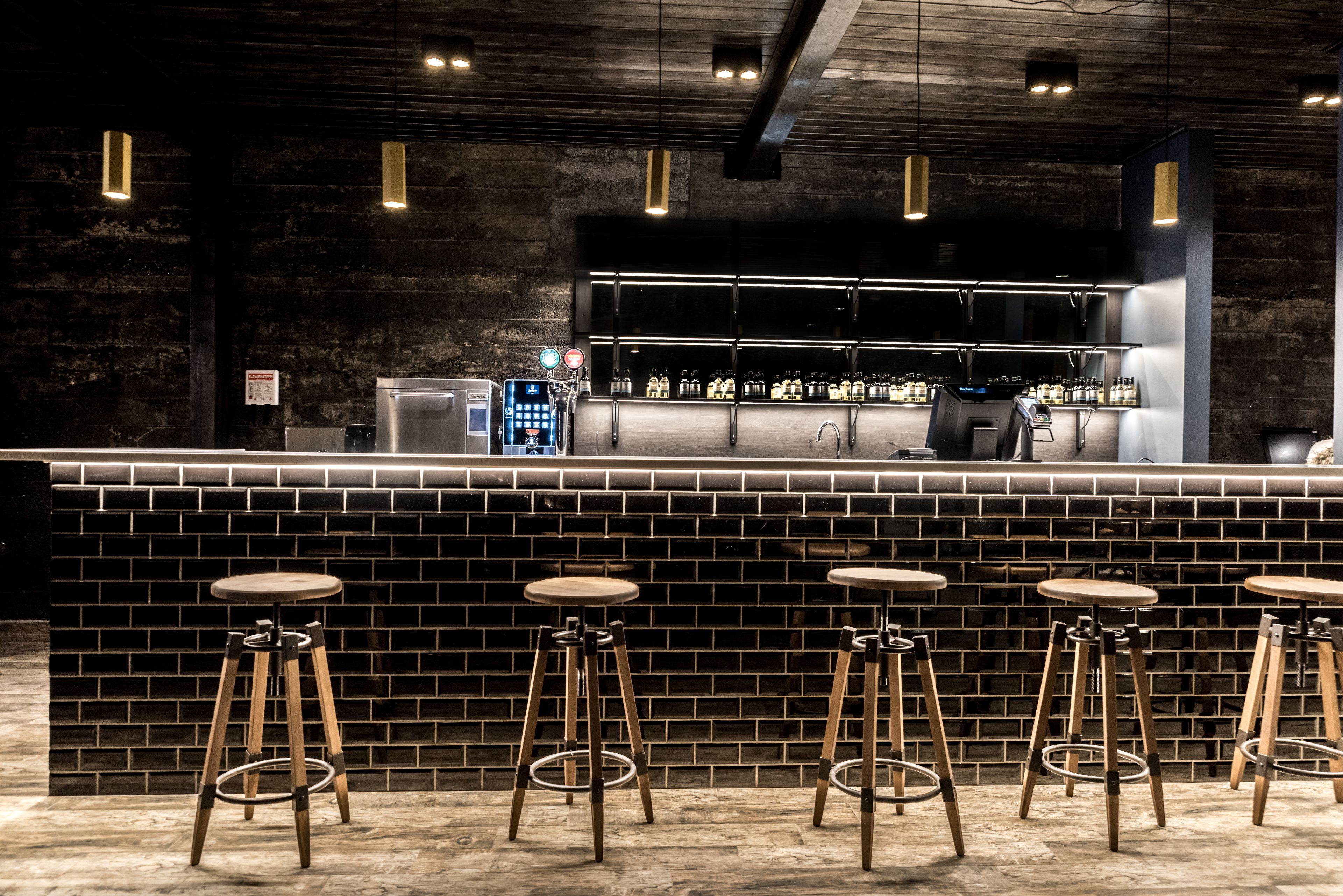 A bar area with a brick wall, stools, and a counter with bottles.