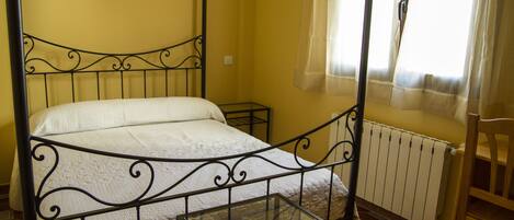 Una cama con dosel y una mesa de vidrio en una habitación con paredes amarillas y un radiador.