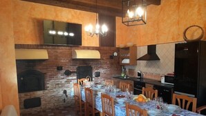 A cozy dining area with a brick fireplace, wooden chairs, a table set for four, and a kitchen with modern appliances. - El Horno de Leopoldo (Hueva)