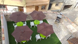 A patio area with green artificial turf, surrounded by stone walls and featuring several tables and chairs, some with brown umbrellas. - El Horno de Leopoldo (Hueva)