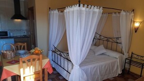 A single bed with a canopy, a dining table with chairs, a kitchen area, and a tiled floor. - El Horno de Leopoldo (Hueva)