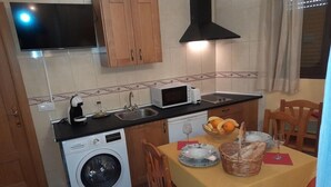 A compact kitchen with a washing machine, microwave, sink, and wooden cabinets. - El Horno de Leopoldo (Hueva)