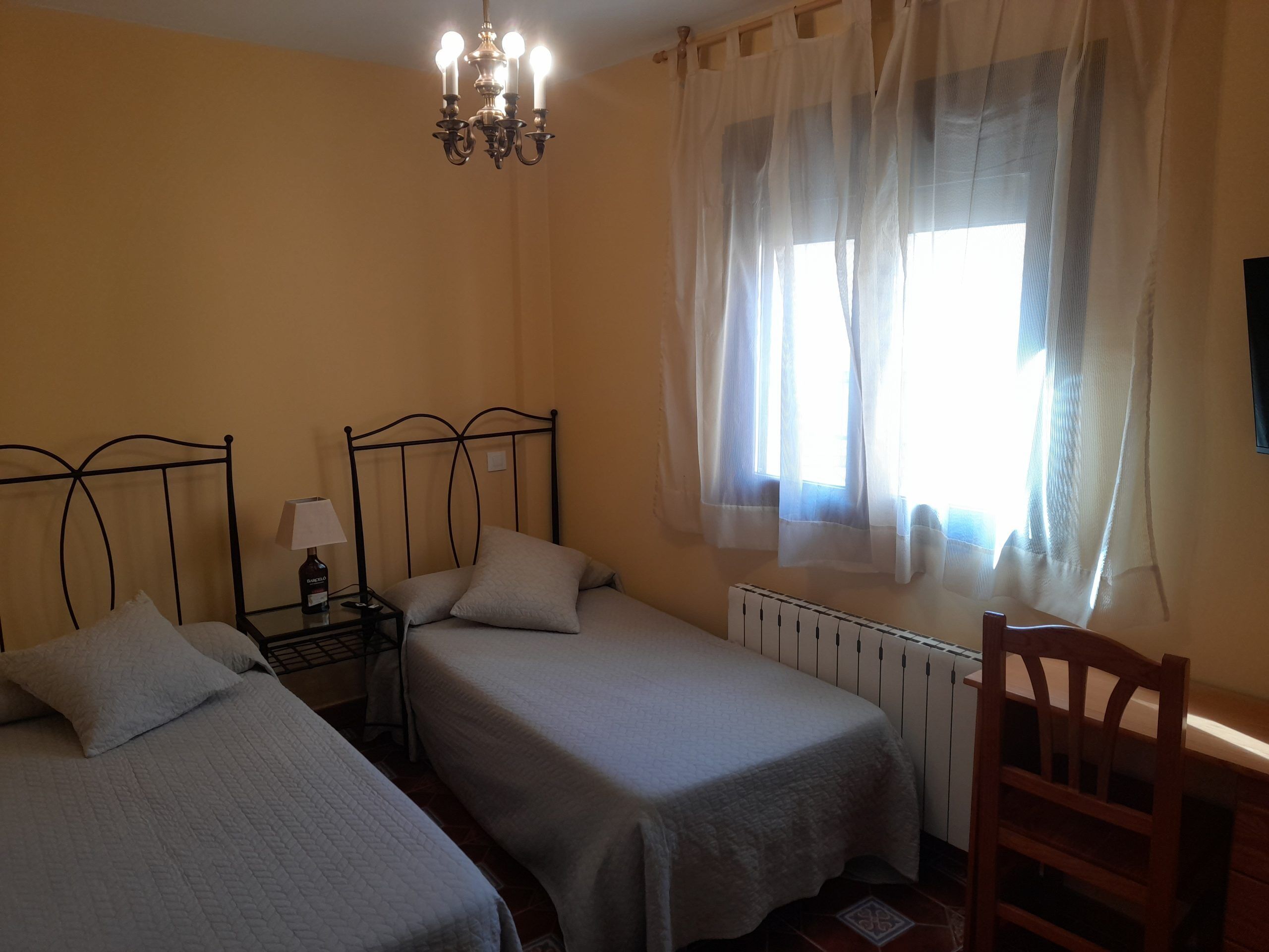 A room with two beds, a radiator, a wooden chair, a lamp, and a chandelier.